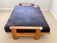 Futon folded flat into bed with pine frame visible at head and foot
