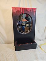 Front view of rectangular black frame mirror with red drip accents and shelf