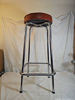 Full view of bar stool front/side showing chrome legs, footrest and padded seat