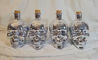 Front view of four silver speckled skull bottles with cork stoppers