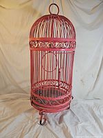 full view of pink metal bird cage showing domed top and feet