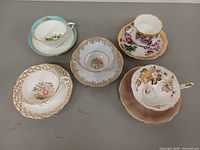 Five teacup and saucer sets arranged, showing overall condition and patterns