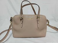 Front view of beige Coach satchel with handles and crossbody strap attached