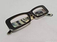 Front three-quarter view of eyeglass frames showing rectangular cut-out lenses and brand on inner lens