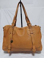 Front view of brown leather tote handbag showing handles, decorative straps, overall shape