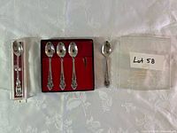 Four ornate Oneida stainless teaspoons in black box with red lining alongside loose packaging