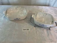 Two Corning Ware casseroles with lids and cradle on table