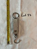 Front view of metal hanging scale beside tape for length reference