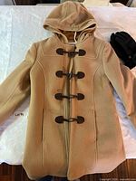 Front view of camel hooded toggle coat with black gloves