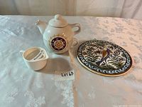 Teapot with cup, egg separator and wall tile displayed together