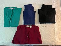 Four folded sweaters: teal cardigan, navy turtleneck, black turtleneck, burgundy vest