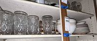 Cabinet shelf with pressed-glass tumblers, stacks of white bowls and plates, additional mugs and glasses visible