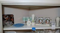 Shelf view showing entire assortment: crystal bowl, blue dish, Belleek vase, Lenox vase, Santa mugs, grape relief vase, ceramic leaf trivet