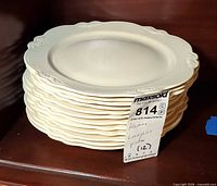 Stack of twelve cream dinner plates with lot tag visible