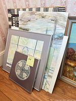 Stack of framed and loose watercolors and a brass rubbing print leaning against wall