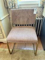 Front view of brass cantilever chair showing dusty-rose chenille upholstery and tufted back