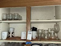 Cabinet shelves showing glass tumblers, wine glass and ceramic mugs