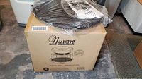 Boxed NuWave oven with sealed lid and accessories on top