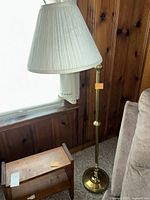 Brass floor lamp with white shade beside wooden table