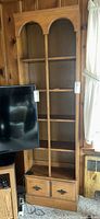 Front view of tall honey oak veneer bookcase beside television