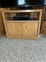Front view of oak TV stand with closed doors and electronics on shelf