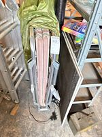 Folded bed showing frame ends and striped mattress with green cover draped