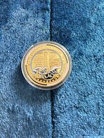 obverse showing gold-tone outer ring, silver-tone field, lighthouse, blue enamel waves, dates, protective capsule