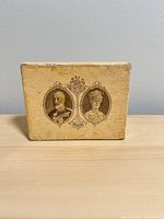 Front of tan slipcase box showing dual royal portraits