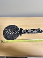 Full view of cast iron key-shaped sign with measuring tape showing length