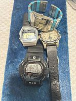 All four wristwatches laid out on blue background showing faces and bands