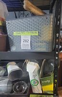 Shelf with grey perforated basket, plastic cups, cartons used as planters