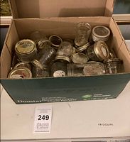 Open box showing multiple glass mason jars with metal lids, various sizes, all visible inside cardboard box