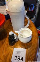 Plastic cat-lidded pitcher, ceramic sugar bowl with spoon, black and white hugging salt & pepper shakers visible on tabletop