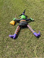 Entire deflated inflatable witch lying on grass showing full figure and extension cord