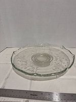 Side view of round clear/frosted etched glass platter showing scalloped rim and central well with ruler for scale