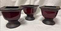 Three burgundy pottery pedestal planters side by side