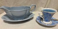 Gravy boat on underplate next to demitasse cup with candle and saucer