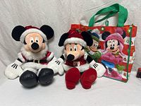 Mickey and Minnie Santa plush seated beside Disney tote bag
