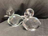 two clear crystal duck figurines side by side on black background