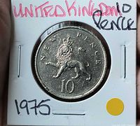 Reverse side of 1975 UK 10 new pence coin in holder showing crowned lion design and handwritten year label