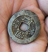 obverse of bronze Chinese cash coin held in hand showing Chinese style characters and square hole