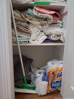 Shelved stack of assorted folded linens above cleaning supplies and toilet paper