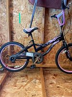 Left side view of 20" pink/black kids bike inside shed