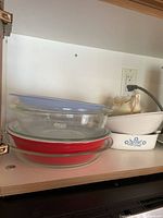 Stacked glass pie plates, oval casserole with plastic lid, CorningWare casserole and gravy boat in cabinet