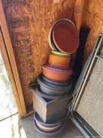 Stack of assorted plastic planters and saucers against shed wall