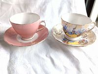 Both teacups with saucers, showing plain pink set and scenic pattern set