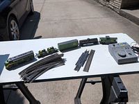 Overview of locomotive, four cars, tractors, track pieces and power pack on table