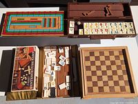 Group view showing cribbage board, rummikub set, scrabble sentence cube box, loose rummy tiles in gold case and wooden chessboard