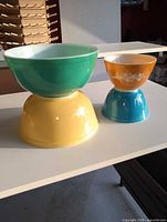 Stacked view of green bowl on yellow bowl, orange bowl on teal bowl