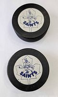 Two St. Catharines Saints logo pucks showing full decals and edge texture